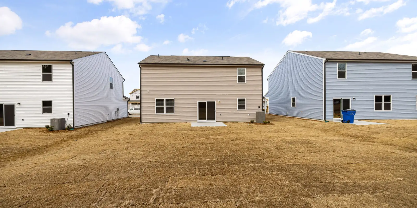 Backyards of single-family homes with dry grass under a blue sky